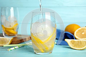 Pouring soda water into glass with lemon slices and ice cubes at light blue wooden table