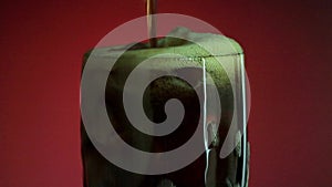 Pouring soft drink in glass with ice splash on red background. Cola or refreshment.