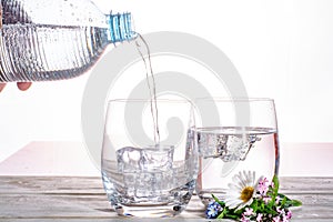 Pouring of sparkling soda mineral drink water in glasses with ice cubes close up copy space