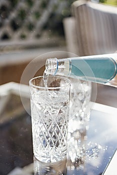 Pouring sparkling water from the bottle into glass. Water drink pouring into glass, garden background