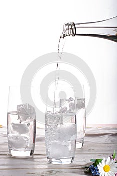 Pouring of stil mineral drink water in glasses with ice cubes cl