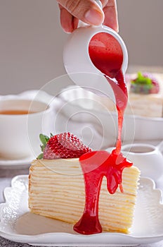 Pouring strawberry sauce onto delicious crepe cake on white plate