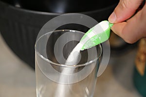 Pouring sugar grains into a clear glass.