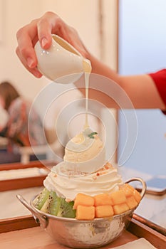 Pouring sweetened condensed milk on top of fruit bingsu.