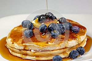 Pouring syrup over the butter on the blueberry stack of pancakes on the kitchen table waiting to be eaten