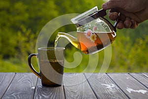 Pouring tea into glass cup on wooden table on blurred background,