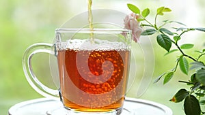 Pouring the tea with leaves of currant, lemon balm, mint, raspberry in a glass cup.Tea party outdoors