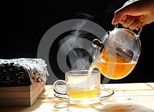 Pouring tea in teapot into a glass,  with steam on wood background