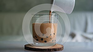 Pouring Thai milk tea with tapioca pearl bubble in glass cup