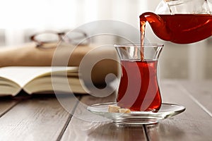 Pouring traditional Turkish tea from pot into glass on wooden table, space for text