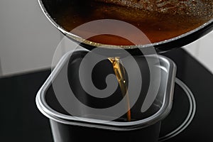 Pouring used cooking oil from frying pan into container