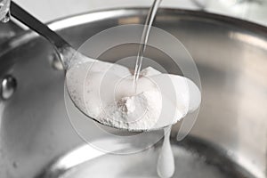 Pouring vinegar into spoon with baking soda