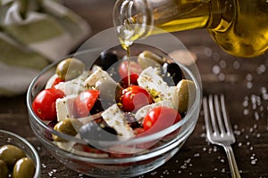 pouring virgin olive oil on vegetarian salad with fresh vegetables, feta and green olives.