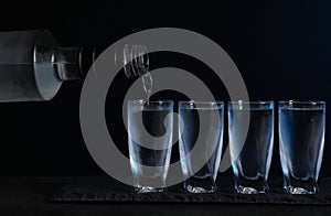 Pouring vodka from bottle in glass on black table