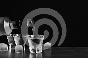 Pouring vodka from bottle in glass and ice cubes on grey table. Space for text