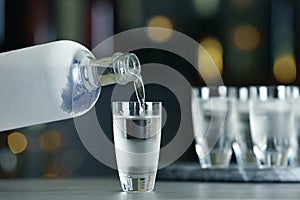 Pouring vodka from bottle into shot glass on counter