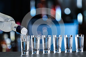 Pouring vodka from bottle into shot glasses on counter