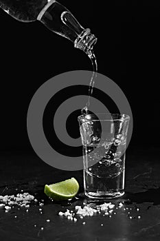 Pouring vodka into the shot glass on a black background with a blank space for a text