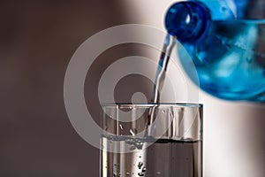 Pouring water from blue plastic bottle into a glass on blurred background. Selective focus, shallow DOF and copy space