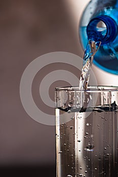 Pouring water from blue plastic bottle into a glass on blurred background. Selective focus, shallow DOF and copy space