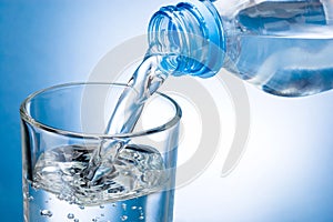 Pouring water from bottle into glass on blue background