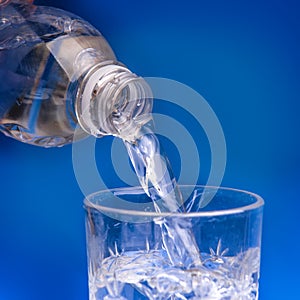 Pouring water from bottle into glass on blue background