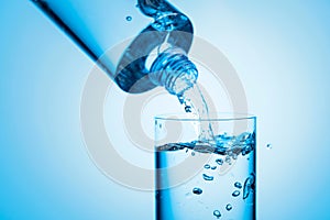 Pouring water from a bottle into glass on a blue background