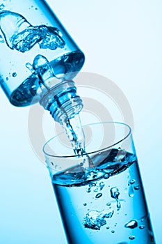 Pouring water from a bottle into glass on a blue background