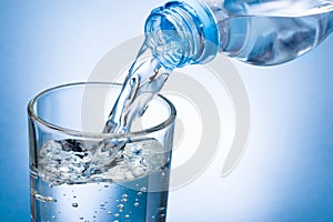 Pouring water from bottle into glass on blue background