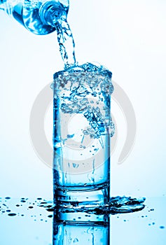 Pouring water from a bottle into glass on a blue background