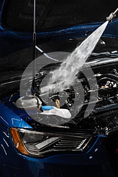 Pouring water on car engine. Washing car engine with spray, brush and detergent in detailing auto service. Detailing