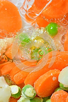 Pouring water on fresh soup vegetables with carrots, peas, cauliflower and corn on white background. Frozen soup