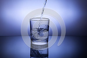 Pouring water into a glass against the blue background