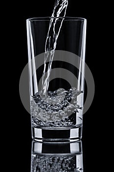 Pouring water into glass on black background