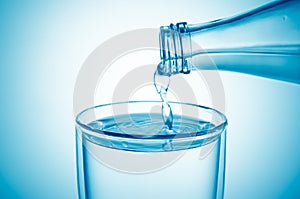 Pouring water from a glass bottle into a glass on blue background, closeup