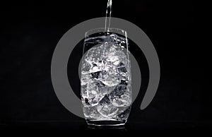Pouring water in glass with crushed ice on black background