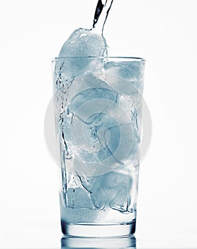 Pouring water in a glass full of ice cubes, white background, blue toned object