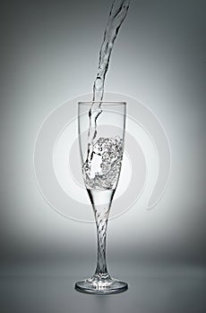 Pouring water into a glass on gray background.