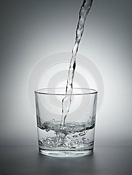 Pouring water into a glass on gray background.