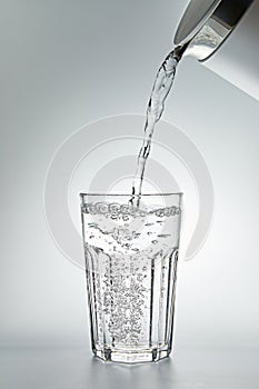 Pouring water into a glass on grey background