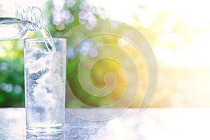 Pouring water into a glass of ice on blurred natural green background