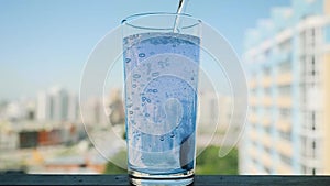 Pouring water in glass with pill in slowmotion. Aspirin splash, headache solution on blurred city background