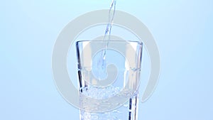 Pouring water in glass, slow motion. Clean and purified water concept, on a a light blue background.