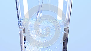 Pouring water in glass, slow motion. Clean and purified water concept, on a a light blue background.