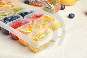 Pouring water into ice cube tray with different fruits