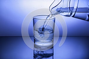 Pouring water from jug into glass on blue background