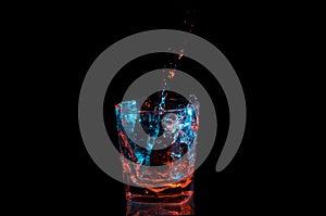 Pouring water into a rocks glass under blue and orange lights isolated on a black background