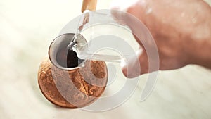 Pouring water into traditional turkish copper coffee pot cezve