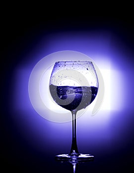 Pouring water into wine glass with black background blue white balance