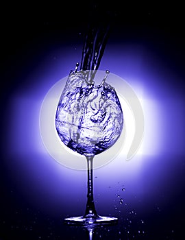 Pouring water into wine glass with black background blue white balance